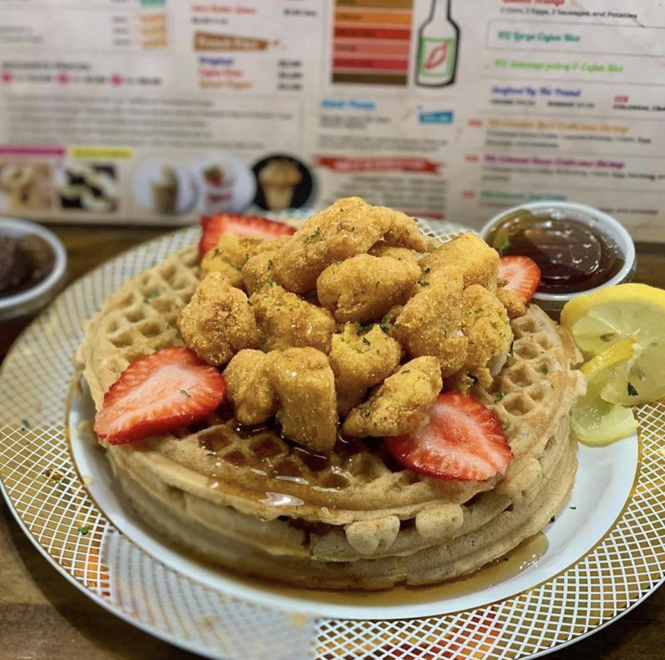 A waffle topped with fried fish and strawberries.