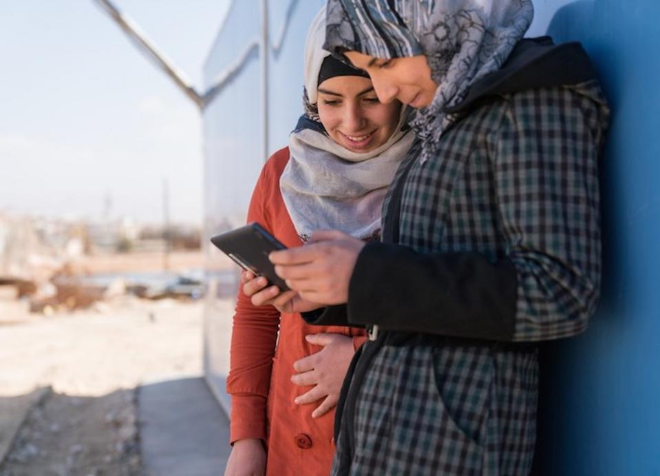Two Syrian refugees use a mobile phone at the Za'atari camp in Jordan. With the launch of its new Cryptofund, UNICEF aims to build institutional knowledge and prepare for a digitally financed future.