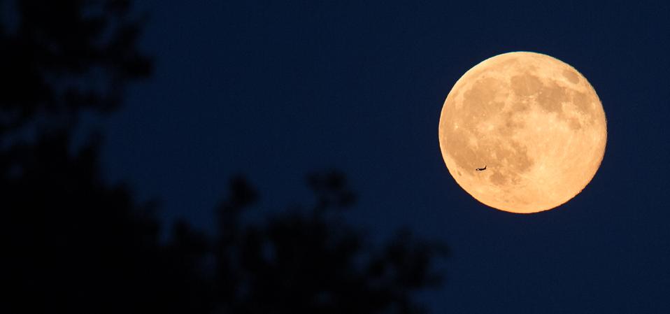 A plane is seen flying in front of a full moon.