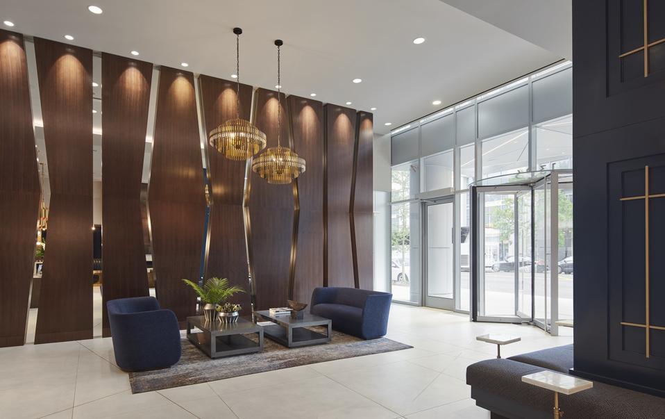 A wall of deep mahogany wood with mirrored cut-outs flanks the lobby interior, reminiscent of the glass angles on the building's exterior.