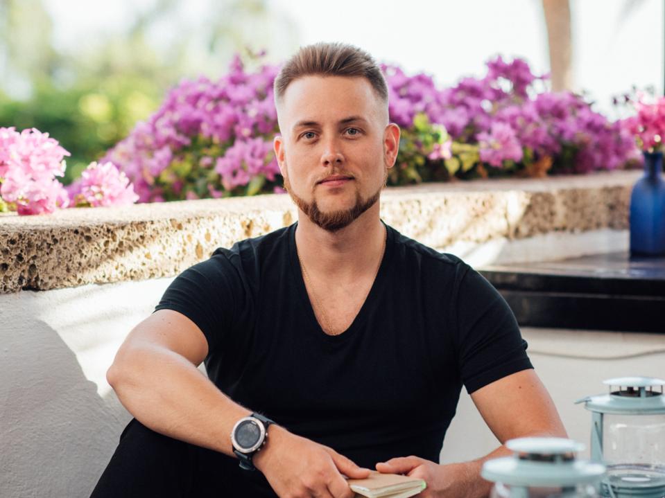 Simo Suoheimo sitting on a sofa with flowers and palm trees behind him.