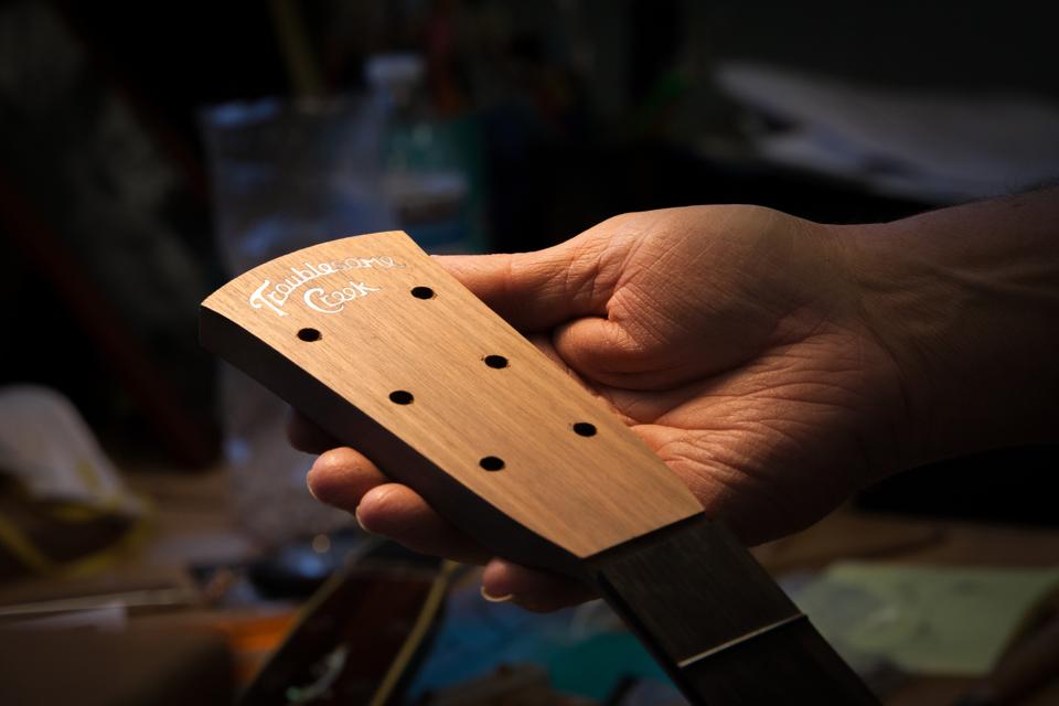 Doug Naselroad, of the Appalachian Luthiery School, hold a partially made guitar head with the Troublesome Creek logo.