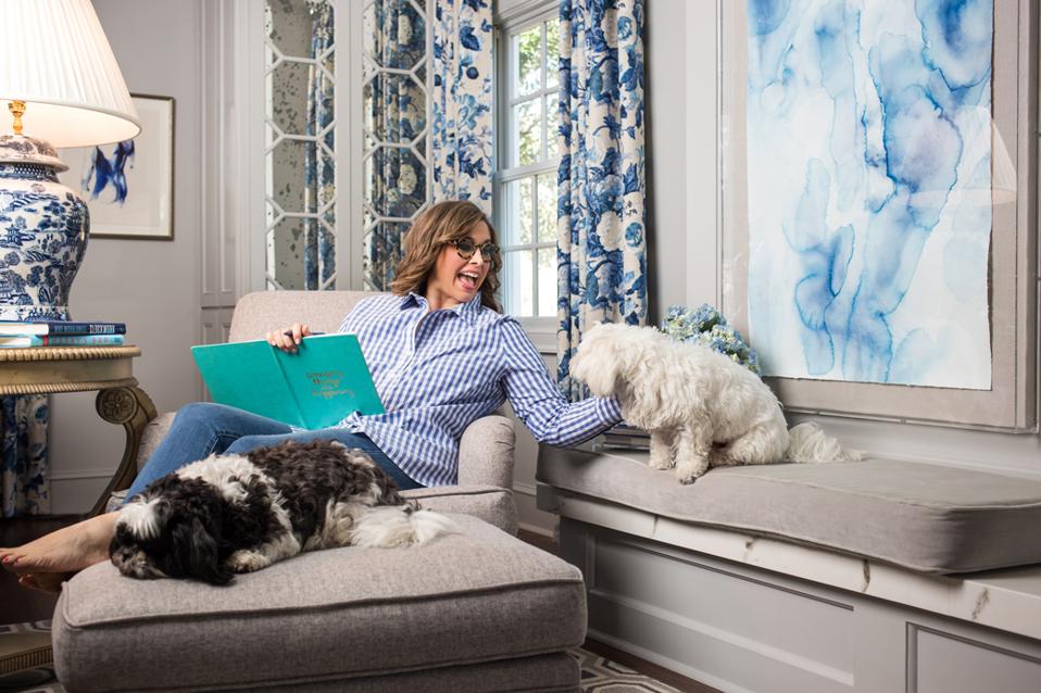 woman in living room reading a book and playing with dogs