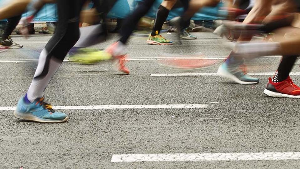 A close-up of runners' feet as they run down a paved street.
