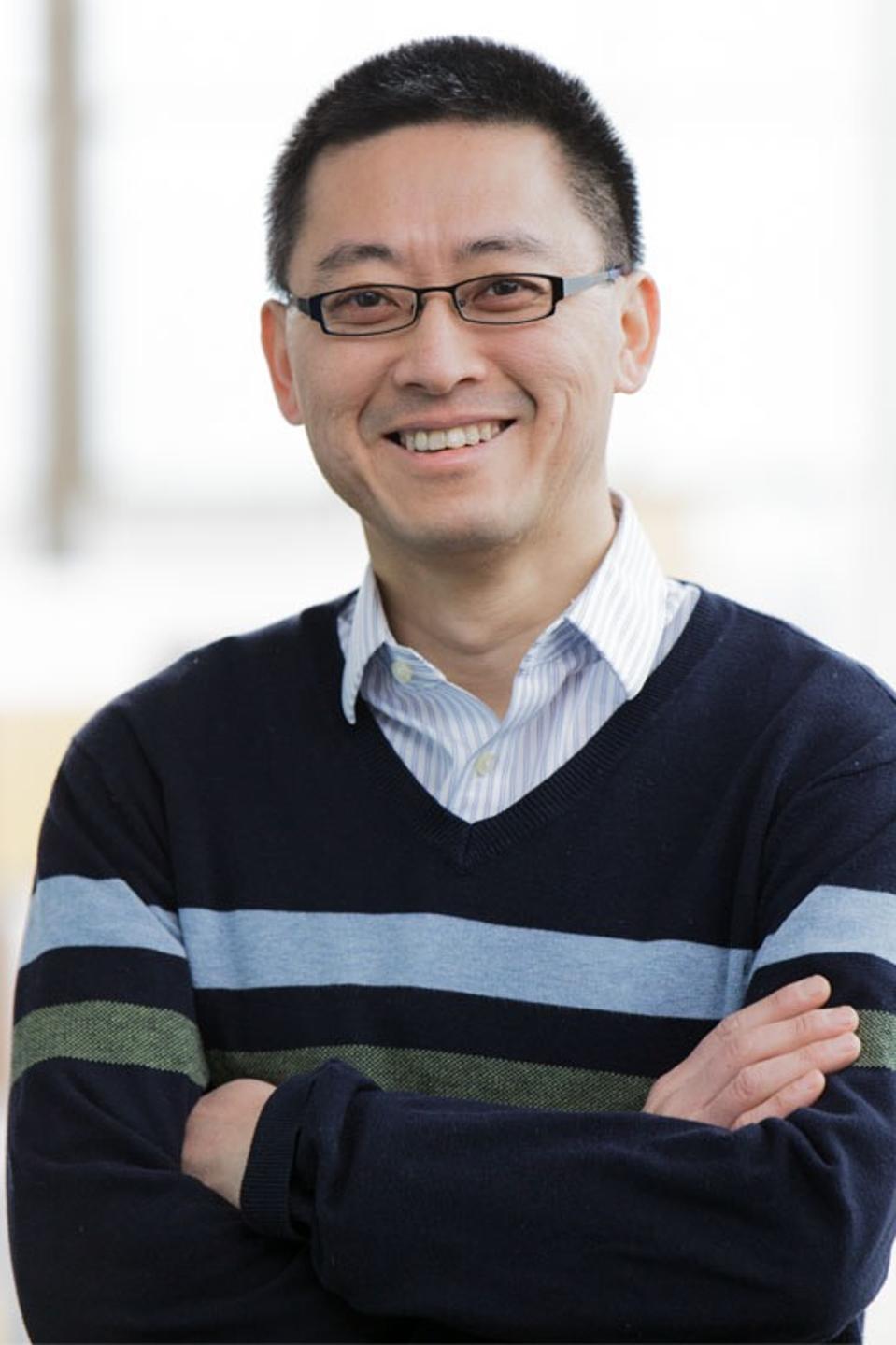 smiling man wearing eyeglasses and striped sweater with arms folded across his chest