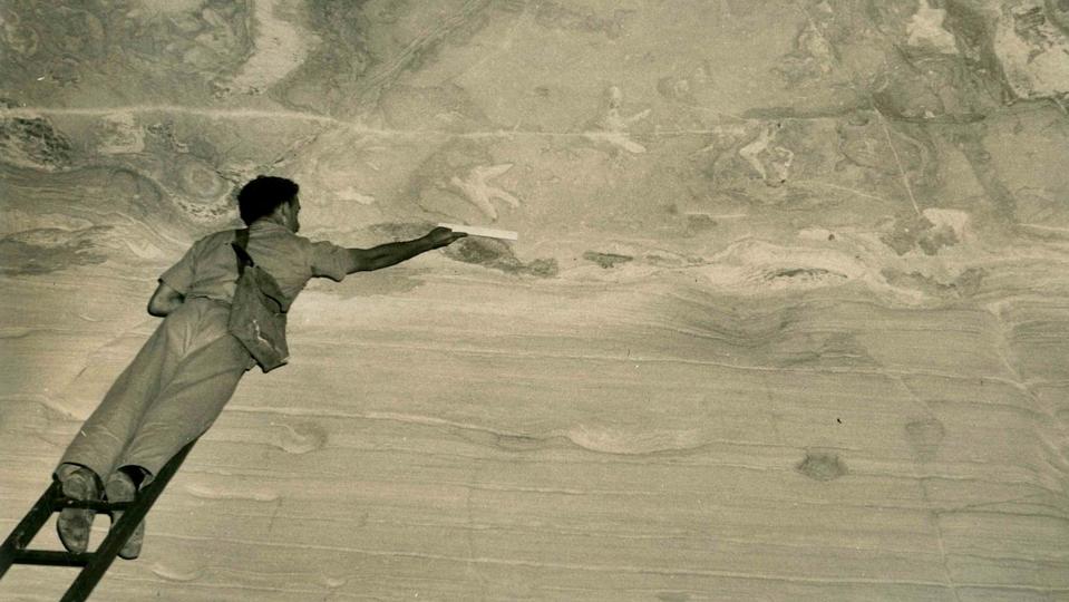 Grayscale photograph of a man on a ladder measuring dinosaur tracks.