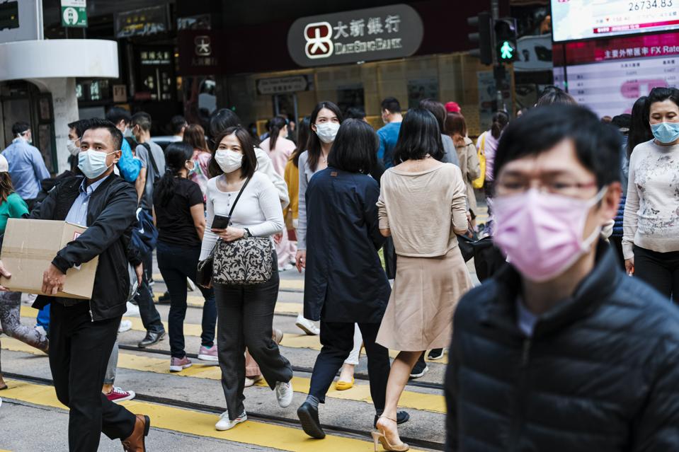 People with surgical face masks cross the street in Central...