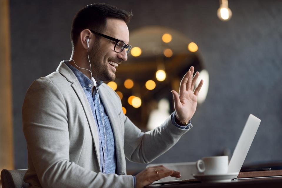 A smiling businessman waves to his computer during a video call.
