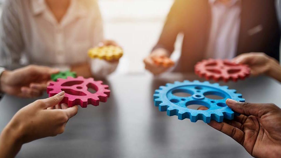 Hands holding different colored gears at a table.