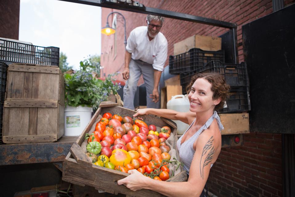 Farmers unloading crates of organic tomatoes outside grocery store