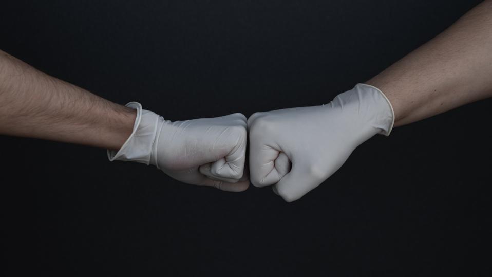 Two hands, covered in medical gloves, fist-bumping