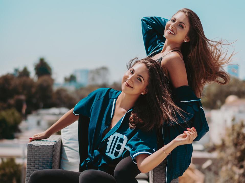 The Wilking Sisters pose in baseball jerseys, Downtown LA skyline in background