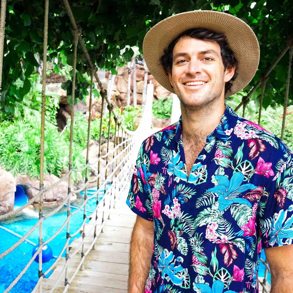 Haisfield stands on a rope bridge in a straw hat with a bright colored shirt.