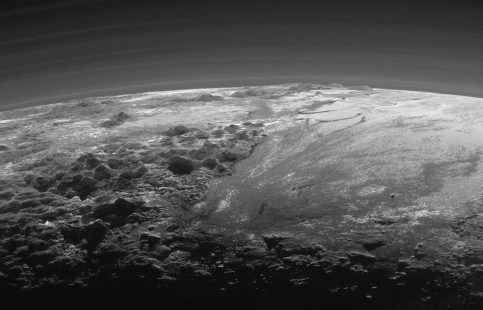 Just 15 minutes after its closest approach to Pluto on July 14, 2015, NASA’s New Horizons spacecraft looked back toward the sun and captured this near-sunset view of the rugged, icy mountains and flat ice plains extending to Pluto’s horizon. The smooth expanse of the informally named Sputnik Planum (right) is flanked to the west (left) by rugged mountains up to 11,000 feet (3,500 meters) high, including the informally named Norgay Montes in the foreground and Hillary Montes on the skyline. The backlighting highlights more than a dozen layers of haze in Pluto’s tenuous but distended atmosphere. The image was taken from a distance of 11,000 miles (18,000 kilometers) to Pluto; the scene is 230 miles (380 kilometers) across.