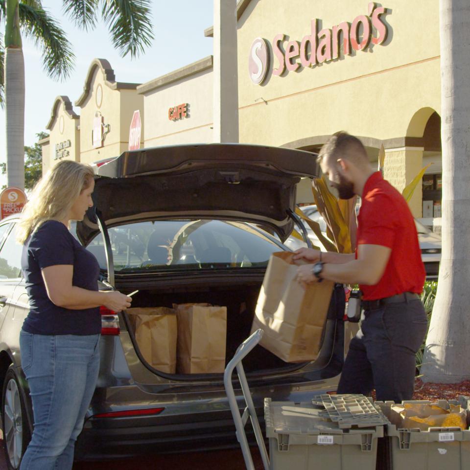 A sales manager from a small supermarket chain, Sedano's, helps a customer load her groceries in her car.