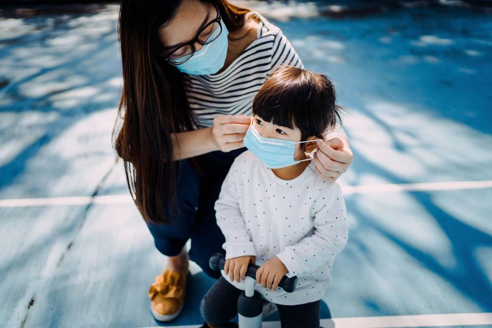 A mom wearing a mask helps a child put a mask on.
