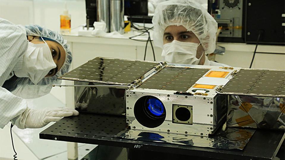 Color photo of two people in PPE working on a cubesat.