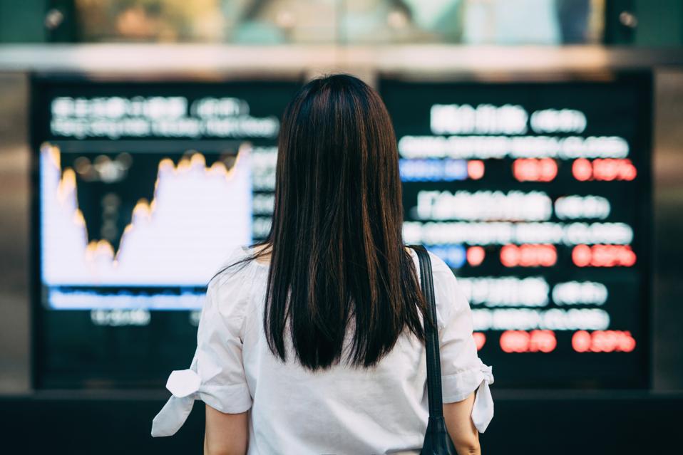 Rear view of businesswoman looking at stock exchange market display screen