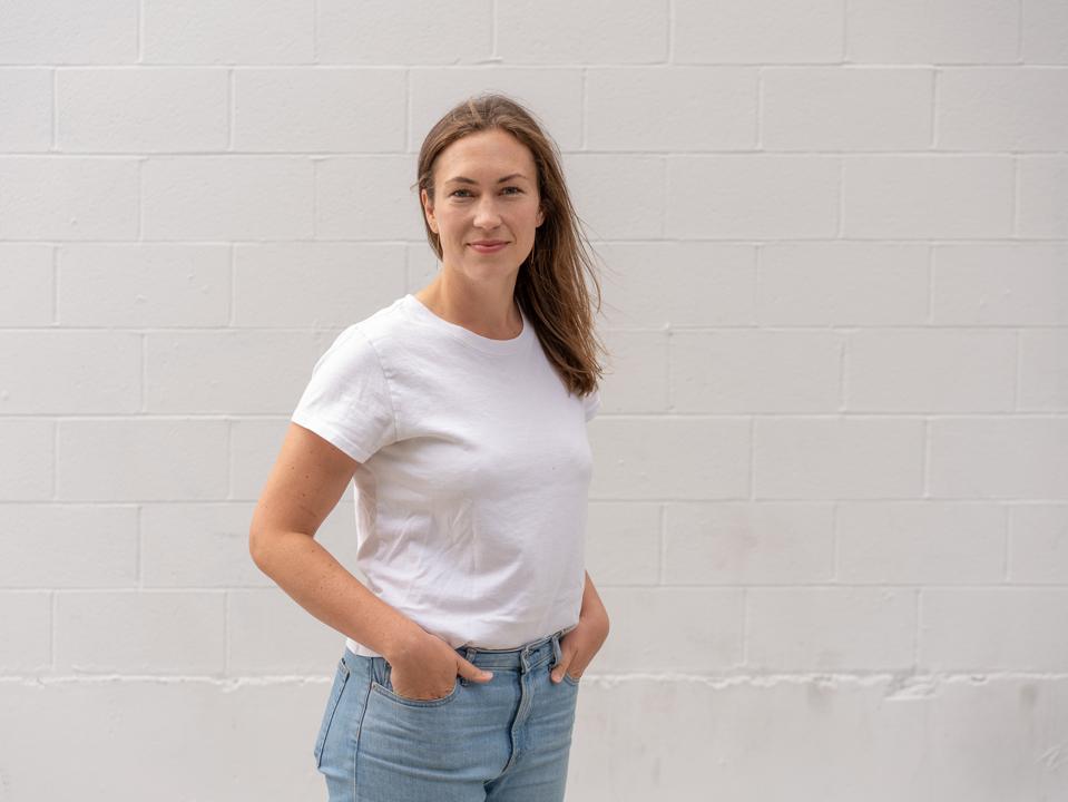 McDevitt, in a white t-shirt, stands in front of a white wall. 