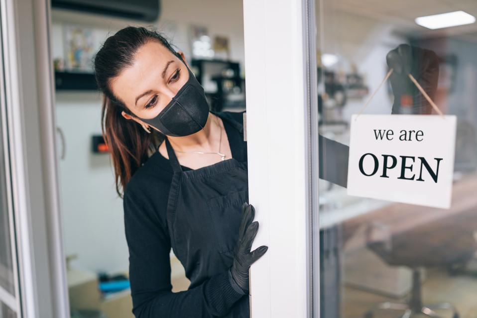 A woman wearing a mask opens the door to her business.