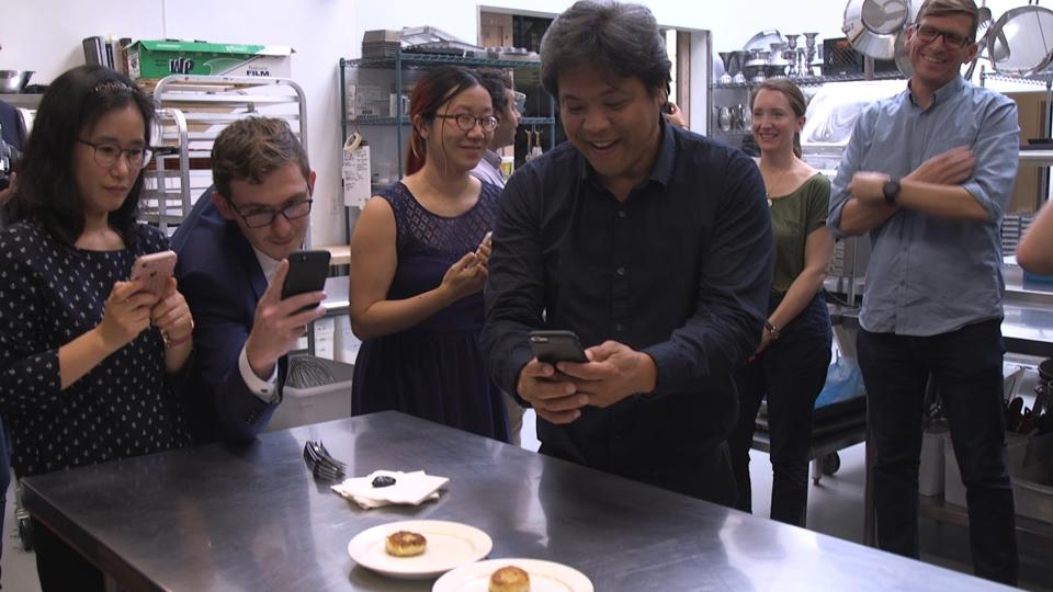 A group of tasters taking pictures of fishcakes made from cultured fish in a test kitchen.
