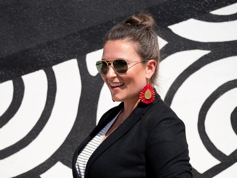 Miller, in sunglasses and Period Movement earrings, stands by a black and white wall