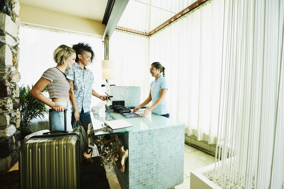 Smiling lesbian couple using smart phone to pay while checking into hotel