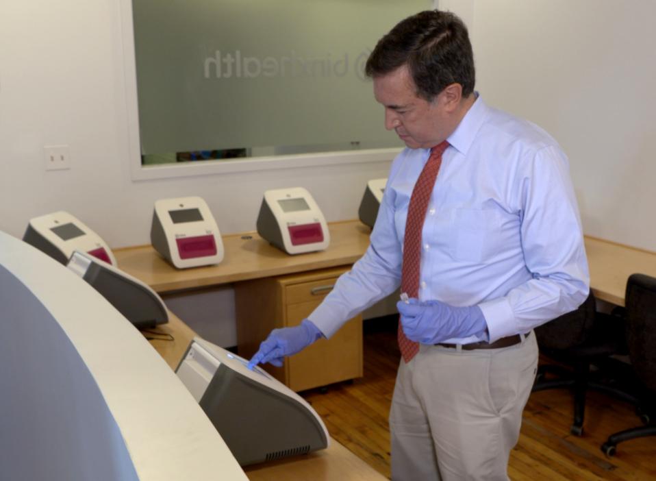 A man in a suit places a patient sample in one of several printer-sized machines to analyze a sample.