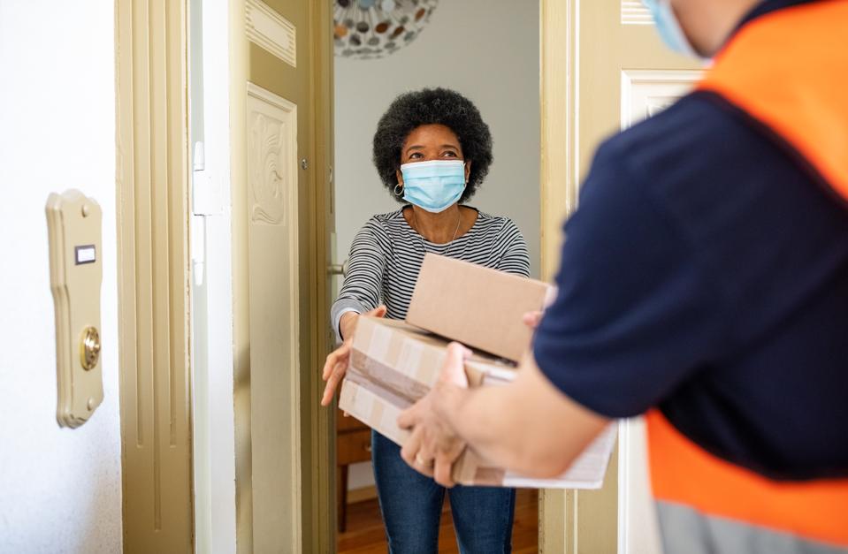 Mature woman getting package from delivery person during pandemic