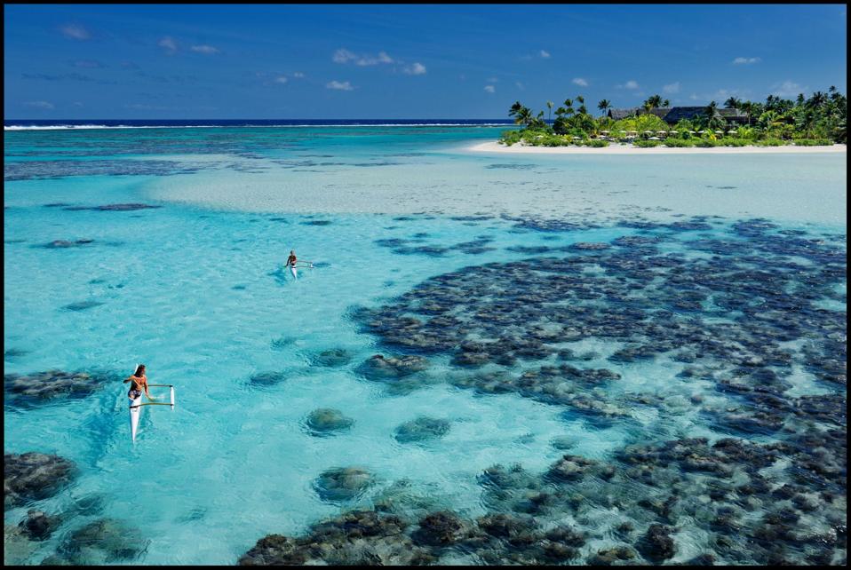 Two kayaks skimming along turquoise water past coral reefs