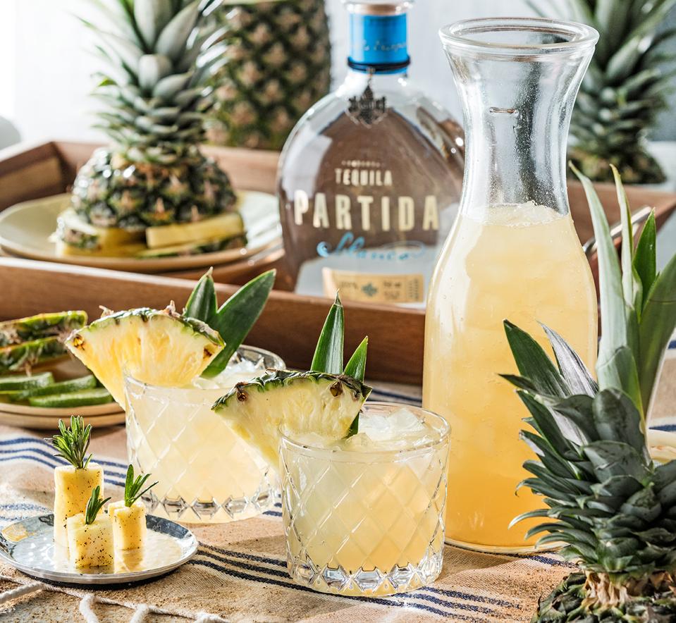 Tequila Partida bottle, pineapples and cocktails in glasses.