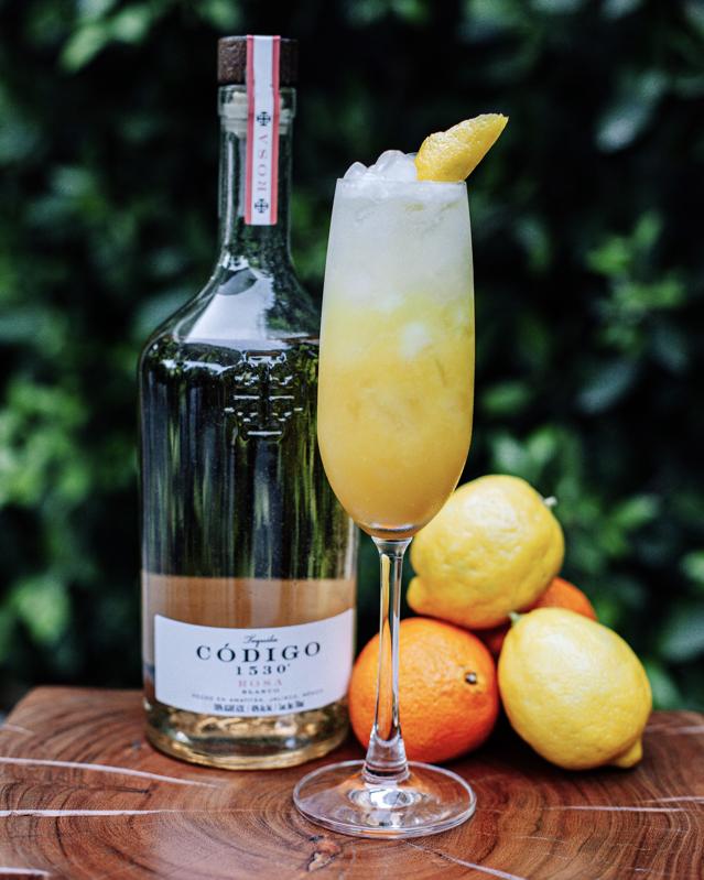 Tequila bottle with cocktail in flute glass and fresh lemons.
