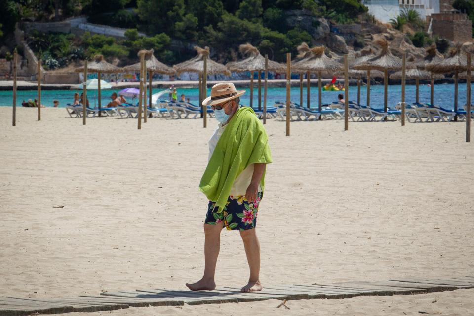 A tourist wearing a face mask walks on Magaluf Beach in Calvia Mallorca Spain