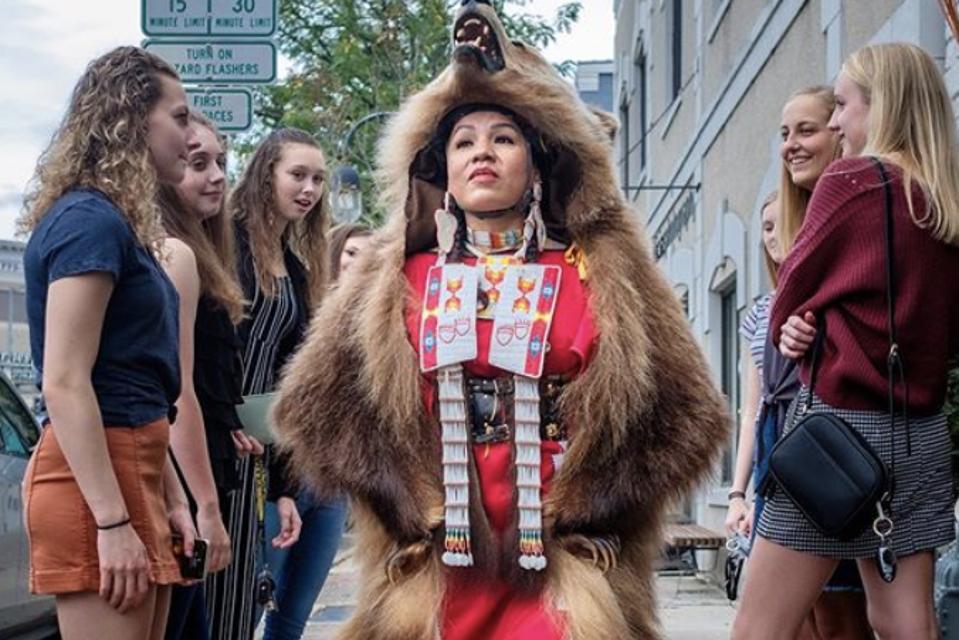 Laura Grizzlypaws walks through a colonized space in her indigenous attire.