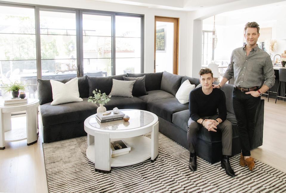 Nate Berkus and Jeremiah Brent sit on a sofa in a living room.