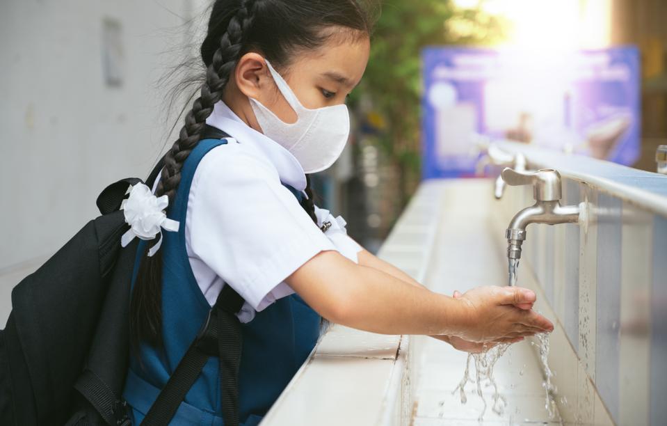 Schoolgirl wearing a face mask while washing her hands.