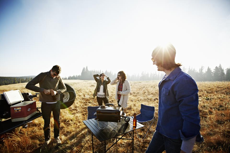 Group of friends barbecuing in field at sunset
