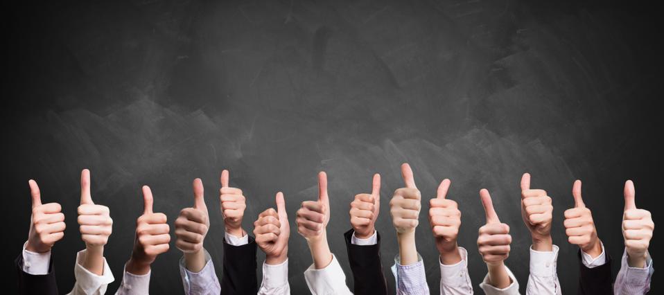 many thumbs up in front of a blackboard, a symbol of employees bonding and collaborating