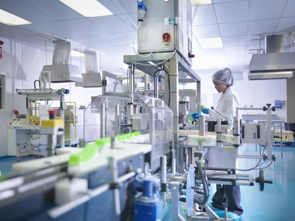 Worker inspecting products on production line in pharmaceutical factory