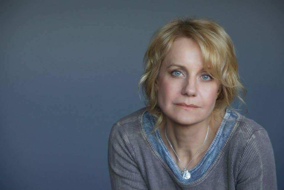 Eileen Grubba poses for a photograph wearing a gray and blue shirt.