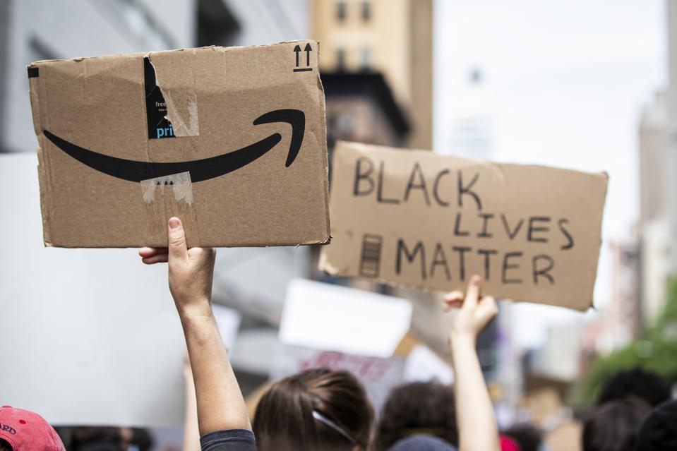The Amazon logo hangs in the air next to ″Black Lives Matter″ signs. Protesters walked from Foley Square to Washington Square Park for a peaceful moment of reflection for those that have been killed.