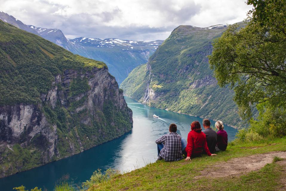 Four people sitting on the ground looking at the Geirangerfjord in Norway.