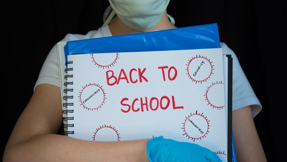 Close-up of student wearing face mask and surgical gloves, holding school books with Back to School written on cover