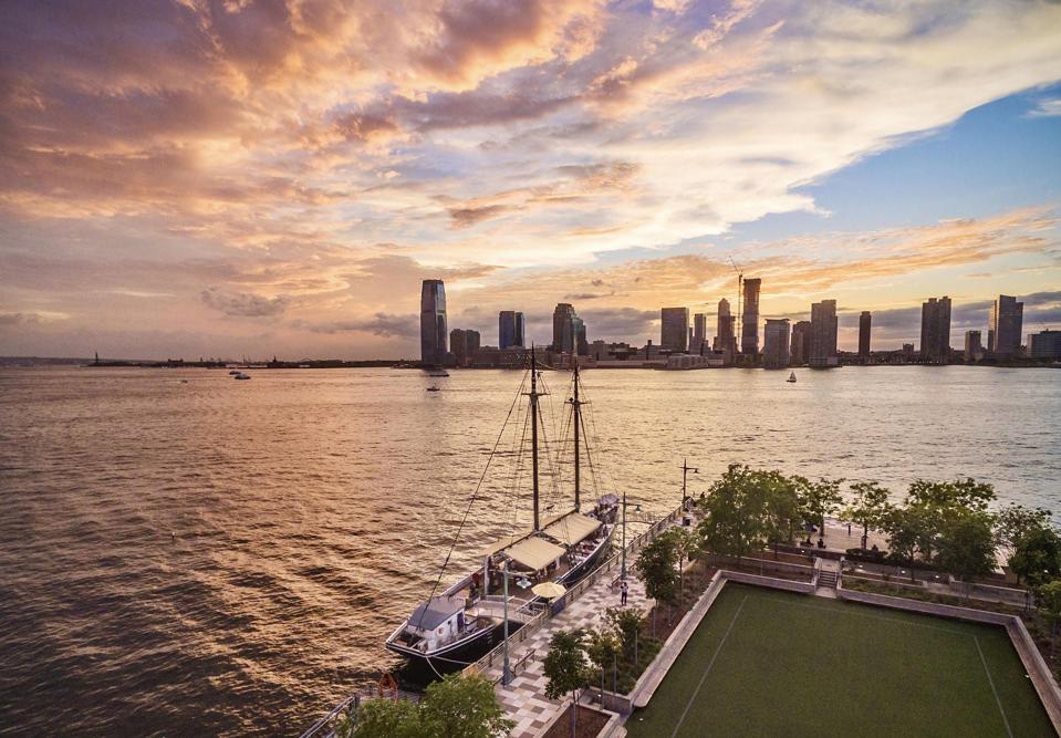 A schooner on New York's Hudson River with the Jersey City skyline in the distance at sunset