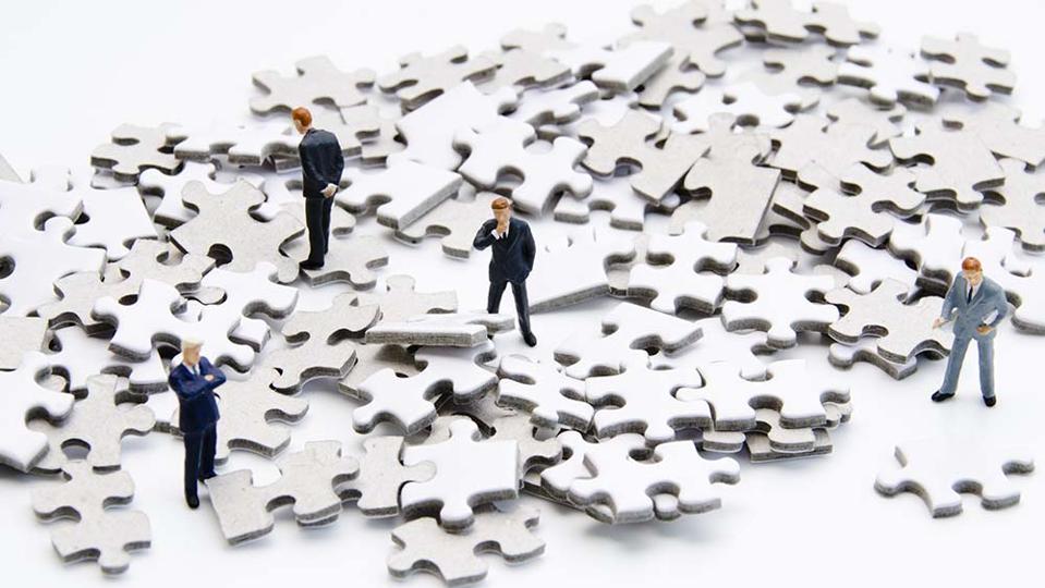 A pile of puzzle pieces with small businessmen figurines examining the pile.