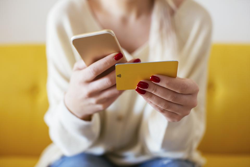 Blonde woman using smartphone and using bank card at home