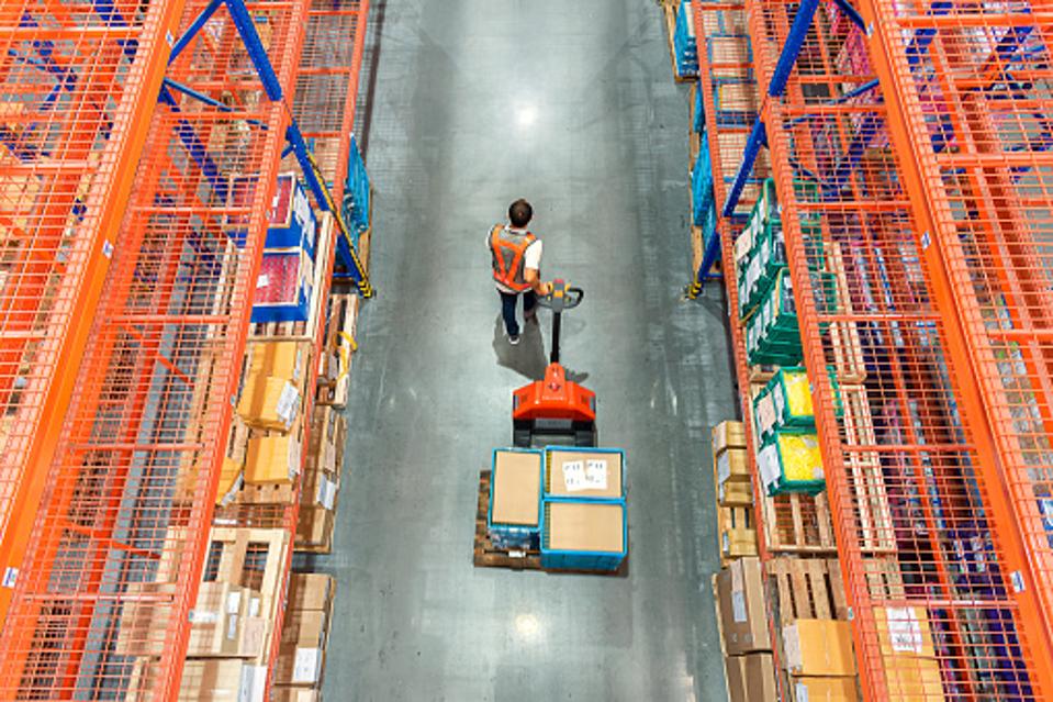 Man hauling a stack of boxes through a manufacturing warehouse.