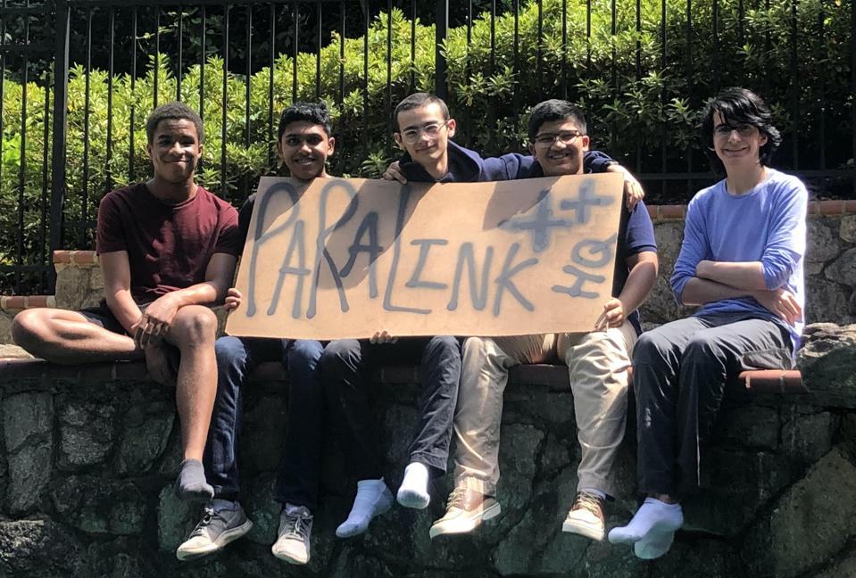 Five teenage boys hold a cardboard sign.