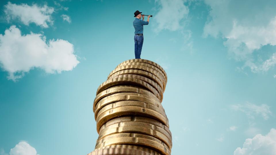 Man standing on stack of coins and looking at telescope