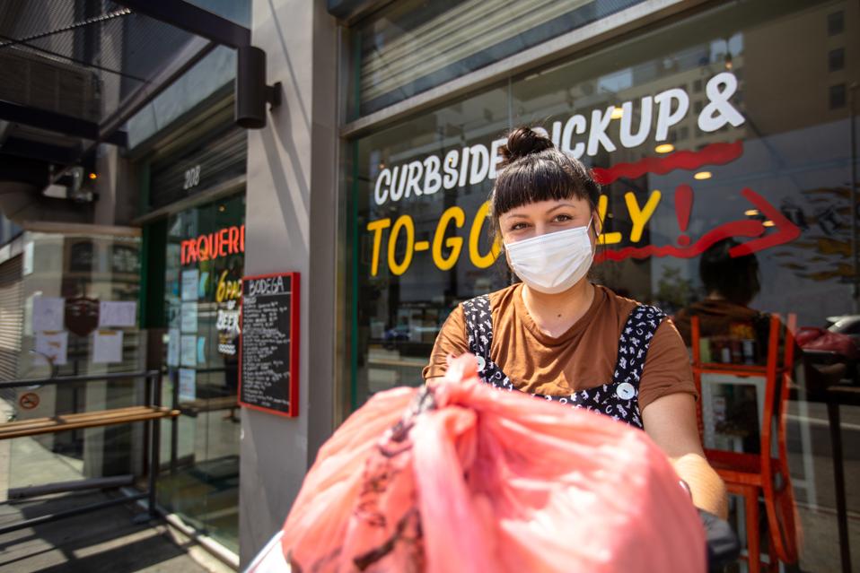 Masked Restauranteur During Covid-19 Lockdown Holding Out Bagged Order to Camera